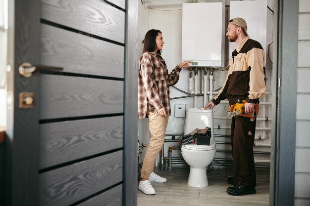 Loodgieter en vrouw staan in een badkamer en bespreken een probleem met sanitaire apparatuur