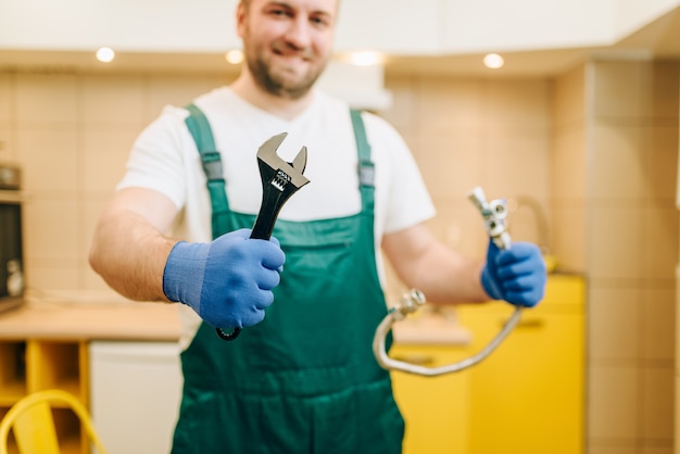 Loodgieter in uniform houdt moersleutel, klusjesman. Professionele werker voert reparaties uit in het hele huis, reparatieservice aan huis