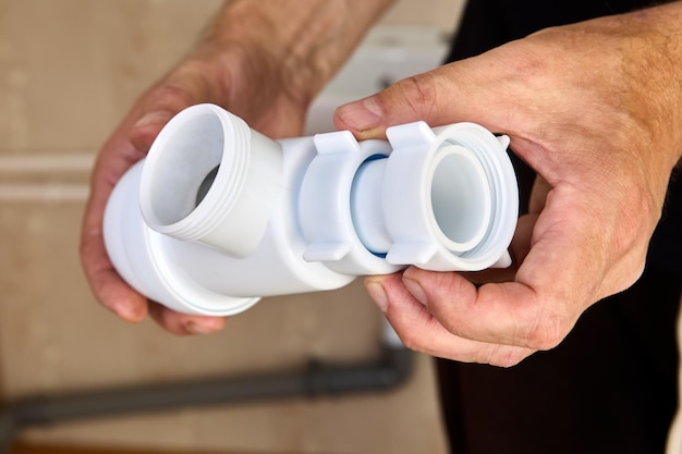 Loodgieter inspecteert lekkende plastic sifon uit gootsteenafvoer in badkamer