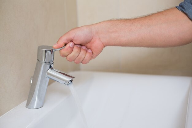 Loodgietershand die een waterkraan openen bij badkamers