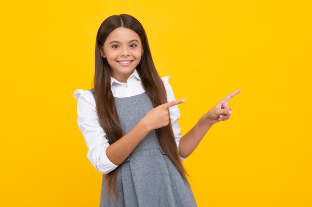 Look at advert Teenager child points aside shows blank copy space for text promo idea presentation poses against yellow background Happy girl face positive and smiling emotions