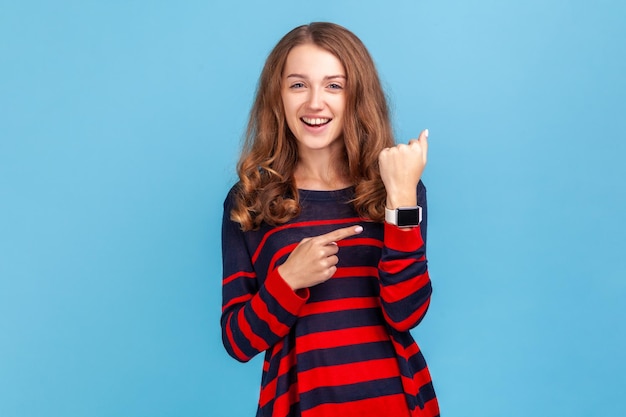 Guarda l'orologio senza fretta ritratto di donna positiva che indossa un maglione in stile casual che punta l'orologio da polso ed esprime ottimismo sul tempo non occupato