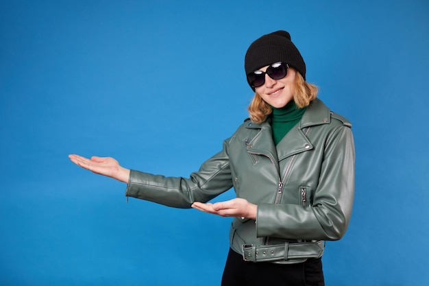 Look at commercial proposal Cheerful woman pointing at copy space on her palm empty place for idea presentation product advertising Indoor studio shot isolated on blue background