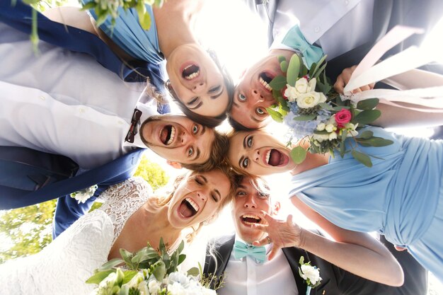 Look from below at funny newlyweds and their friends bending to the camera