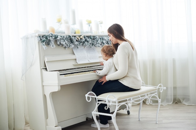 Look from behind at mother and daughter playing white piano