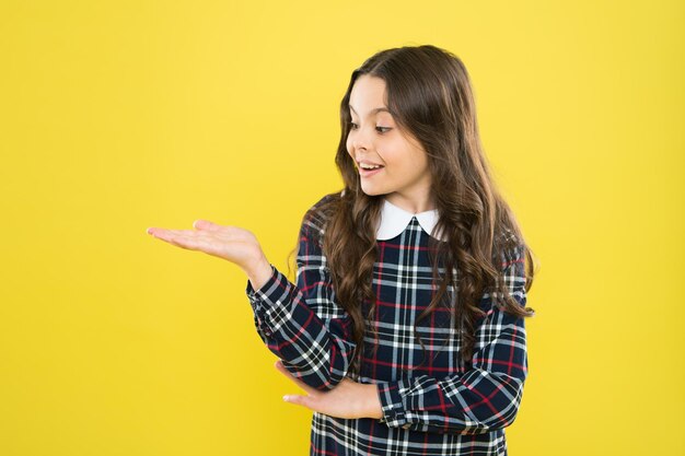 Look here Product presentation Small girl nice hairstyle Child long curly hair Happy schoolgirl stylish uniform Happy childhood concept Happy smiling kid portrait Emotions emotional expression