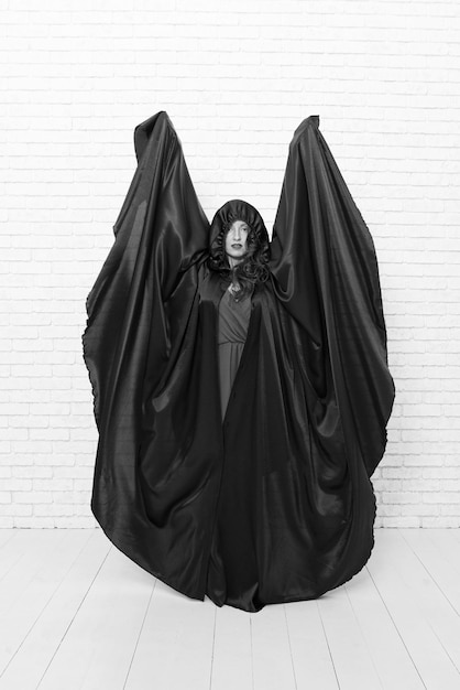 Посмотрите, это мой костюм на Хэллоуин Чувственная женщина, одетая как ведьма Хэллоуина на белой кирпичной стене Сексуальная девушка в черной тоге для вечеринки в честь Хэллоуина Подготовка и празднование Хэллоуина