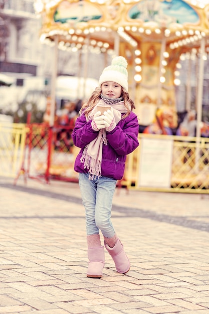 Look at me. Cute girl holding paper cup in both hands and looking straight at camera