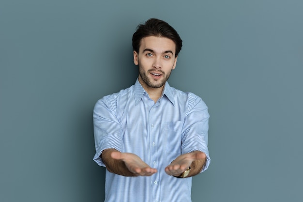 Photo look at me. nice positive attractive man stretching out his hands and showing them to you while standing against grey background