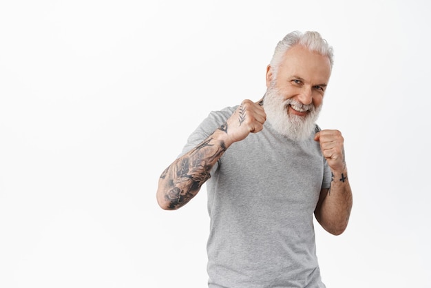 Look at my jab Smiling playful senior man wants sparring standing in boxing boxer pose and ready for fight looking happy as fool around standing over white background