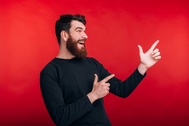 Look, smiling bearded man is pointing with both hands on red wall