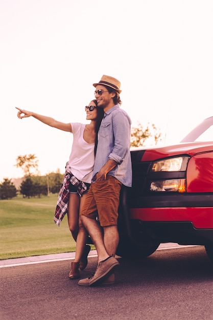 Look at that! Full length of beautiful young couple bonding to each other and leaning at their pick-up truck while woman pointing away and smiling
