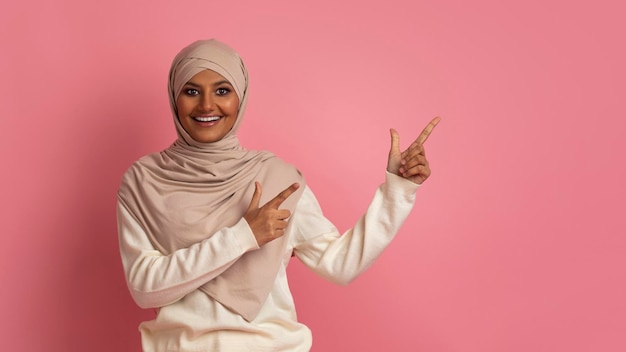 Look There Beautiful young muslim woman in hijab pointing at copy space