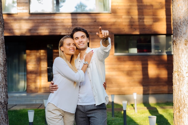 Look there. Positive cheerful man hugging his girlfriend while pointing with her hand