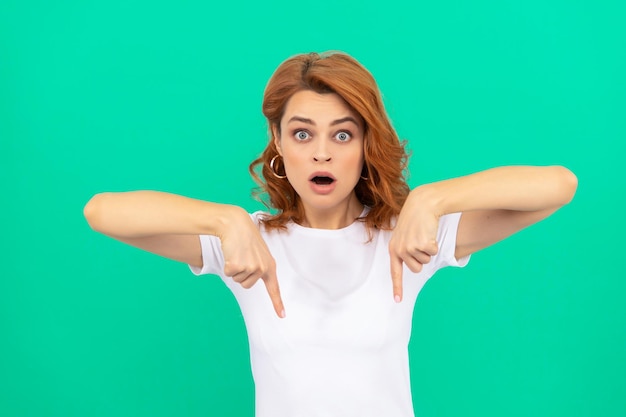 look there. shocked woman with curly hair point finger down. beauty and fashion. female fashion model. pretty look of young girl. portrait of redhead lady on blue background. express emotions.