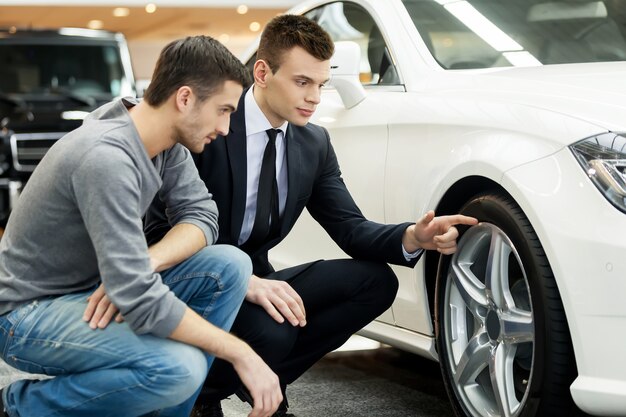 Look at these tires! Young car salesman showing the advantages of the car to the customer