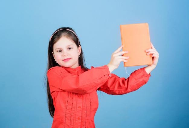 Look at this book Small pupil took the book from library Adorable school child with activity book Cute little girl holding note book with orange cover copy space