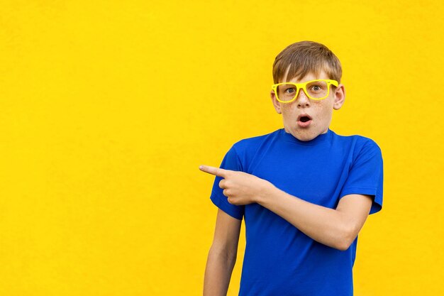 Look this handsome young child in shoked pointing away while standing isolated on light yellow