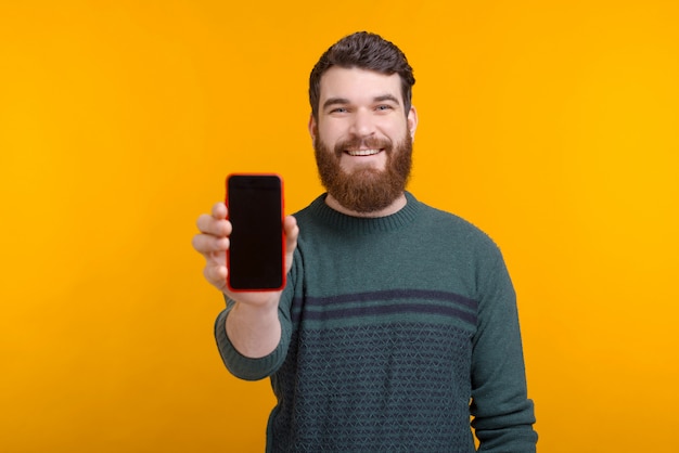 Look at this online offer or ad. Handsome man is showing his phoneâs blank screen on yellow space.