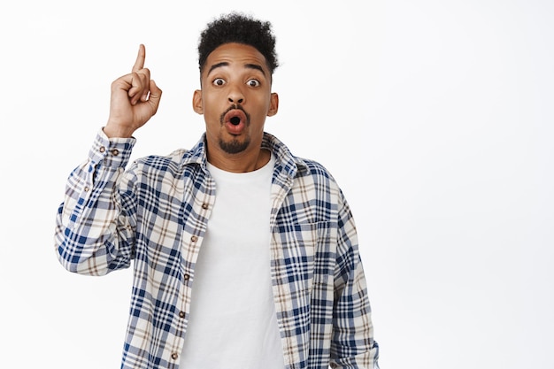 Look up. Excited african american guy tell big news, has suggestion, raising finger up eureka gesture and saying his idea plan, standing against white background