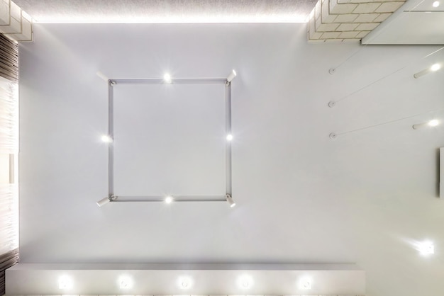 Look up on suspended ceiling with halogen spots lamps and\
drywall construction in empty room in apartment or house stretch\
ceiling white and complex shape