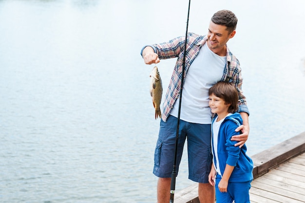 Look what we caught! Father holding fishing rod and showing big fish to his son