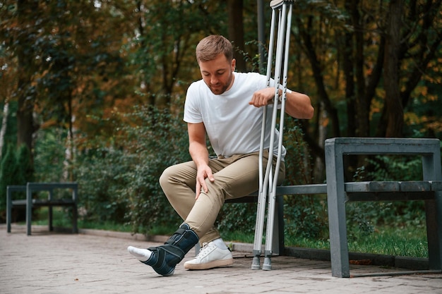 Photo looking at the broken leg man with crutches is in the park outdoors having leg injury