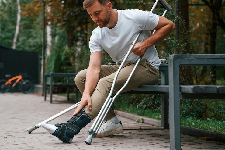 Photo looking at the broken leg man with crutches is in the park outdoors having leg injury