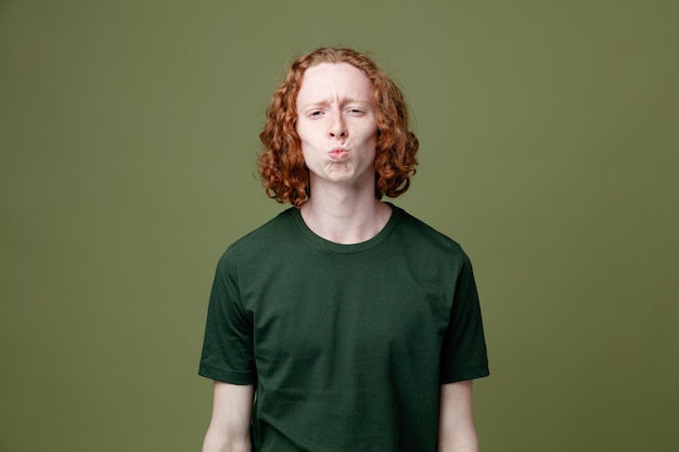 Looking at camera showing kiss gesture young handsome guy wearing green t shirt isolated on green background