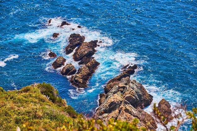 Looking down at ocean from cliffs with boulders and waves crashing