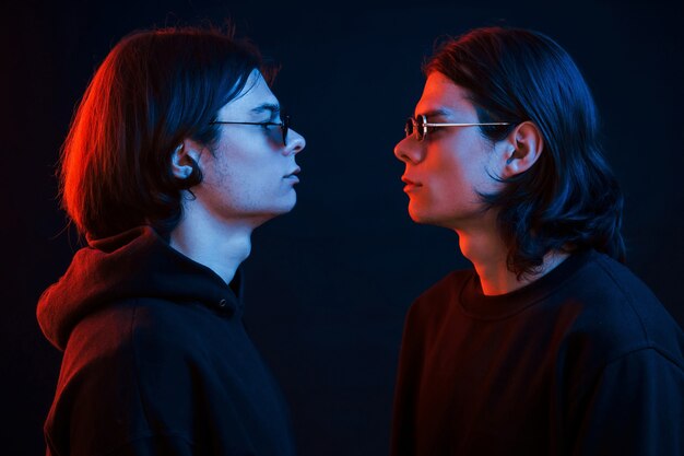 Looking at each other. Creative photo. Portrait of twin brothers. Studio shot in dark studio with neon light.