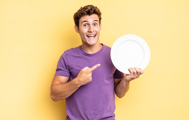 Looking excited and surprised pointing to the side and upwards to copy space. empty plate concept