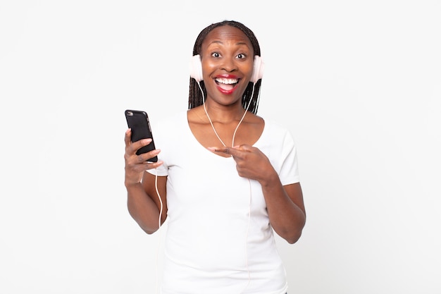 Looking excited and surprised pointing to the side with headphones and a smart phone