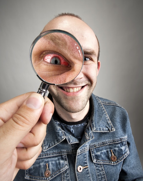 Looking to funny smiling man with angry eye through magnifying lens