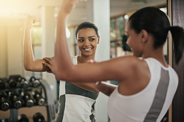 Looking good a young woman flexing her muscles in front of the mirror at the gym