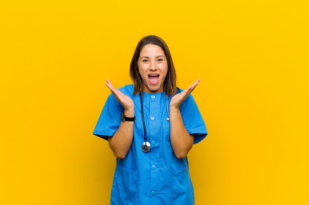 Foto apparentemente felice ed eccitato scioccato da una sorpresa inaspettata con entrambe le mani aperte accanto al viso isolato contro il muro giallo