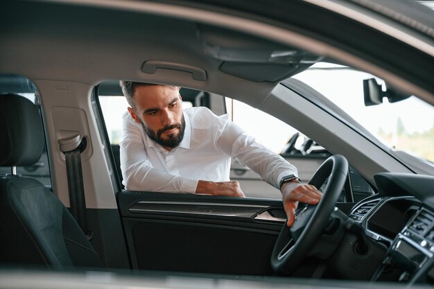 looking inside of the automobile young man in white clothes is in the car dealership