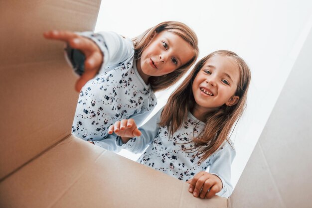 Looking inside of paper box Two cute little girls indoors at home together Children having fun