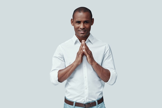 Looking into your heart. Handsome young African man looking at camera and smiling while standing against grey background