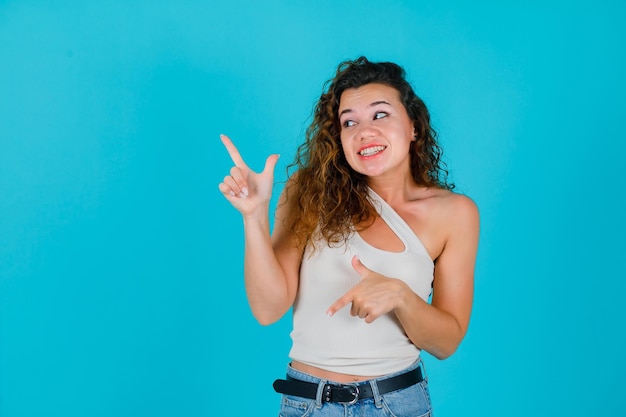 Looking left young girl is pointing left with forefingers on blue background