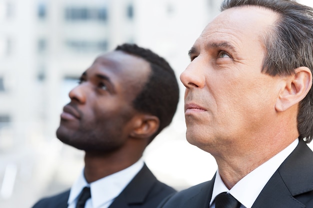 Looking for new opportunities. Side view of two confident businessmen looking up while standing outdoors
