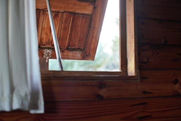 Photo looking out wooden window on beach house, opened just a little bit, blurred bright landscape outside.