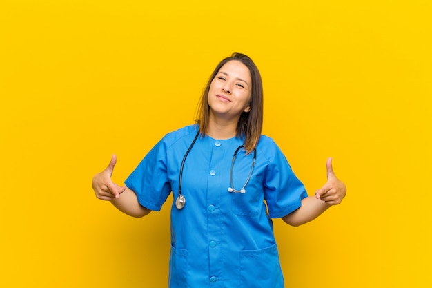 Looking proud, arrogant, happy, surprised and satisfied, pointing to self, feeling like a winner isolated against yellow wall