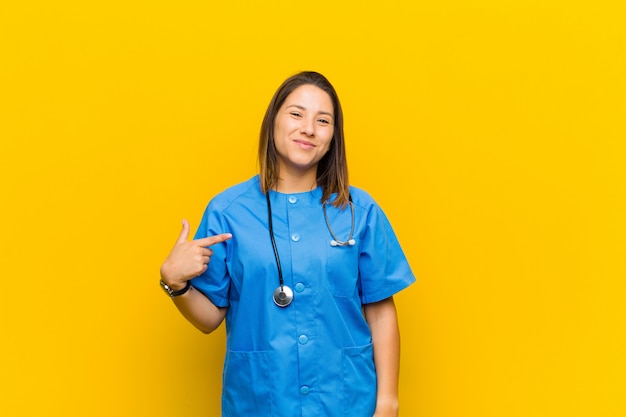 Looking proud, confident and happy, smiling and pointing to self or making number one sign isolated against yellow wall