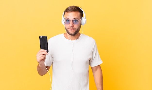 Looking puzzled and confused, listening music with headphones and a smartphone