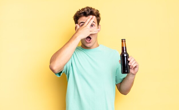 Looking shocked, scared or terrified, covering face with hand and peeking between fingers. beer bottle concept