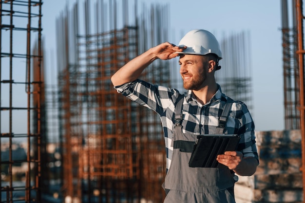 Foto guardando di lato holding tablet l'uomo sta lavorando al cantiere durante il giorno