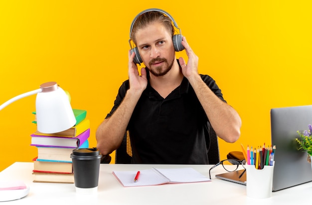 Looking side young guy student wearing headphones sitting at table with school tools 