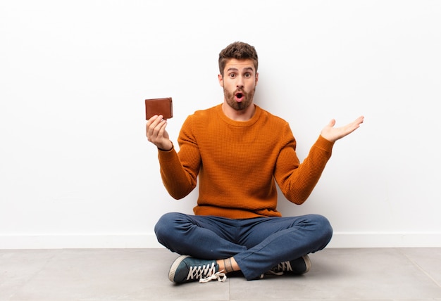 Photo looking surprised and shocked, with jaw dropped holding an object with an open hand on the side holding a wallet