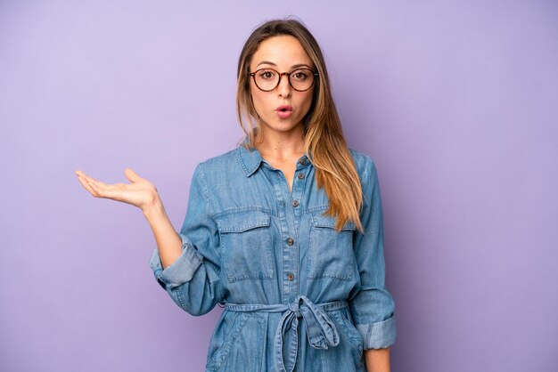 Looking surprised and shocked with jaw dropped holding an object with an open hand on the side